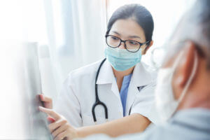 Asian woman Doctor in surgical mask giving advice to old man patient