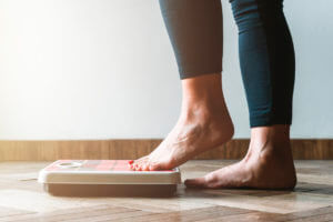A woman wearing leggings and stepping on a scale to track her weight loss.