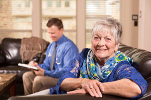 Concierge doctor service. Doctor makes home visit to senior woman at her house or an assisted living facility. House call. Elderly woman in foreground waiting for doctor to finishing writing his report.