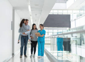 Happy pregnant family taking to a nurse at the hospital and smiling - healthcare and medicine concepts